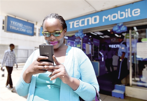 在肯尼亚首都内罗毕市中心，一名女子在一家传音手机专卖店前使用自己的传音手机。10年间，来自中国深圳的传音手机在非洲年销售量从不到100万台增至近8000万台，荣登国产手机海外销量榜首，旗下社交聊天软件注册用户过亿。 （新华社发）